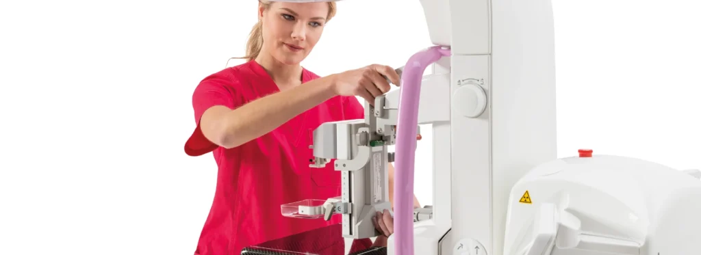Technik w czerwonym uniformie reguluje ramię mammografu Planmed