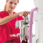 Technik w czerwonym uniformie reguluje ramię mammografu Planmed